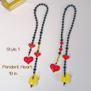 May include: Two black beaded necklaces with red heart and yellow duck charms. The necklaces are 19 inches long. Style 1 has three red hearts and a yellow duck at the bottom. Style 2 has one red heart and a yellow duck at the bottom.