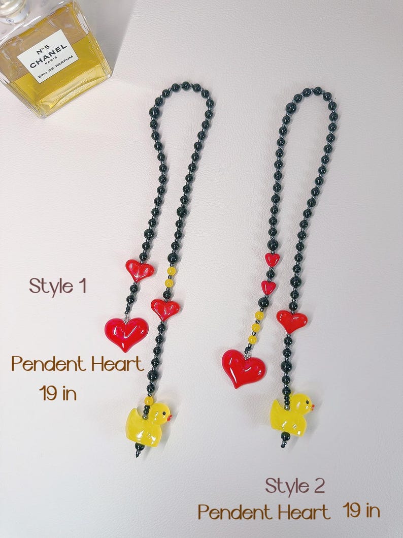 May include: Two black beaded necklaces with red heart and yellow duck charms. The necklaces are 19 inches long. Style 1 has three red hearts and a yellow duck at the bottom. Style 2 has one red heart and a yellow duck at the bottom.