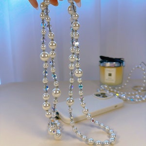 May include: A white pearl and crystal phone charm with a double strand of pearls and iridescent crystals.