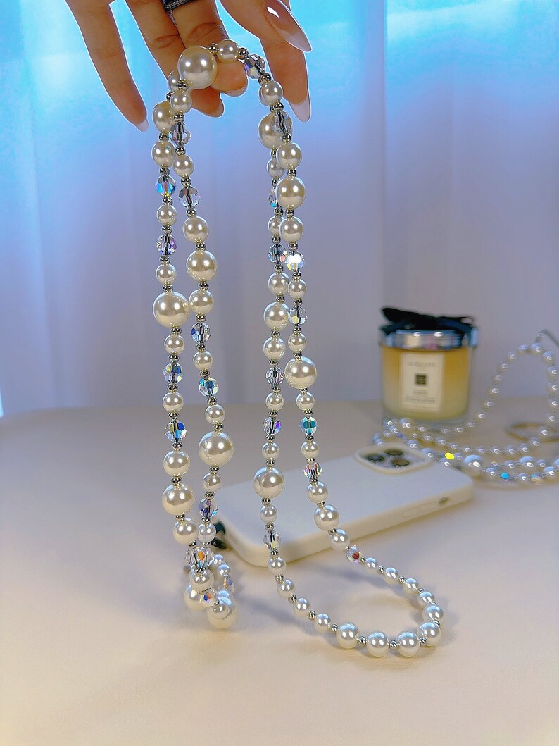 May include: A white pearl and crystal phone charm with a double strand of pearls and iridescent crystals.