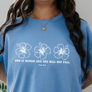 May include: A light blue t-shirt with a white graphic of three hibiscus flowers and the text "God is within her, she will not fall. Psalm 46:5."
