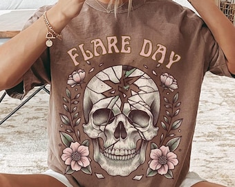 May include: A brown t-shirt with a graphic of a skull with flowers and the text "FLARE DAY" printed on it.