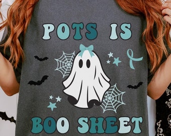 May include: A dark gray t-shirt with a teal and white graphic of a ghost with a bow and the text "POTS IS BOO SHEET".