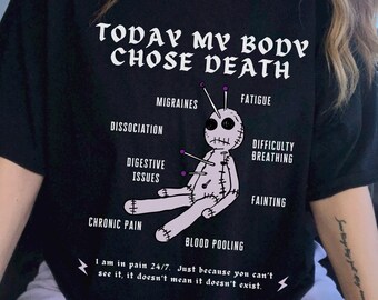 May include: Black t-shirt with a graphic of a voodoo doll with pins in it. The text "TODAY MY BODY CHOSE DEATH" is above the doll. The text "I am in pain 24/7. Just because you can't see it, it doesn't mean it doesn't exist." is below the doll.