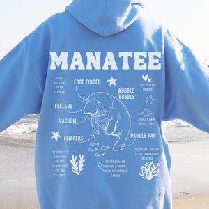 May include: A light blue hoodie with a white graphic of a manatee with anatomical details and the word "MANATEE" in large white letters. The graphic includes information about the manatee's anatomy, such as its flippers, feelers, and paddle pad.