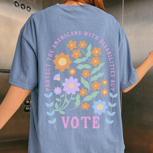 May include: A blue t-shirt with a floral design and the text "Protect the Americans with Disabilities Act" and "Vote" on the back.