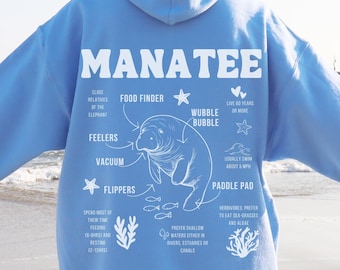 May include: A light blue hoodie with a white graphic of a manatee with anatomical details and the word "MANATEE" in large white letters. The graphic includes information about the manatee's anatomy, such as its flippers, feelers, and paddle pad.