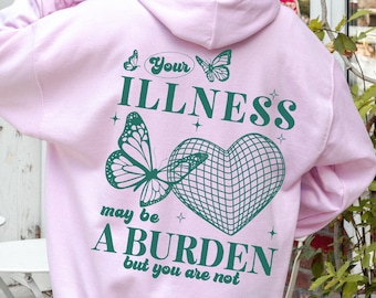 May include: Pink hoodie with a green graphic print of a butterfly and a heart with a mesh design. The text on the hoodie reads "Your illness may be a burden but you are not."