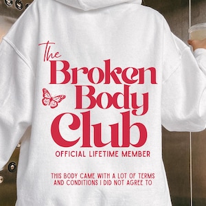 Può includere: Felpa con cappuccio bianca con coulisse e una grande grafica rossa sul retro. La grafica include il testo "The Broken Body Club", una farfalla e le frasi "OFFICIAL LIFETIME MEMBER" e "THIS BODY CAME WITH A LOT OF TERMS AND CONDITIONS I DID NOT AGREE TO."