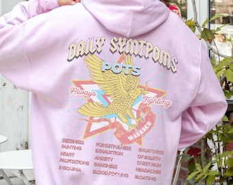 May include: Pink hoodie with a graphic of a golden eagle and the text "Daily Symptoms POTS Always Fighting Warrior". The text "Dizziness, Fainting, Heart Palpitations, Insomnia, Forgetfulness, Exhaustion, Anxiety, Shaking, Blood Pooling, Shortness of Breath, Chest Pain, Headaches, Bloating" is printed on the hoodie.