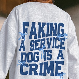 May include: Gray sweatshirt with the text "Faking a service dog is a crime" in blue lettering with blue bows around the text.