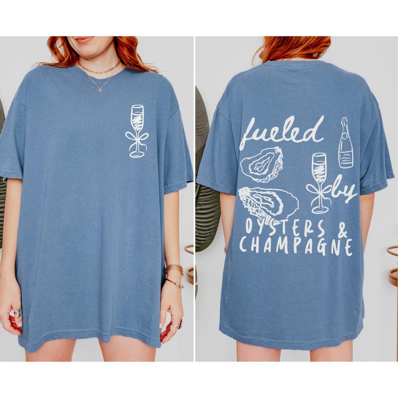Puede incluir: Una camiseta azul con un dise&ntilde;o gr&aacute;fico blanco en la espalda que dice "fueled by oysters & champagne". El gr&aacute;fico incluye ilustraciones de ostras y copas de champ&aacute;n.