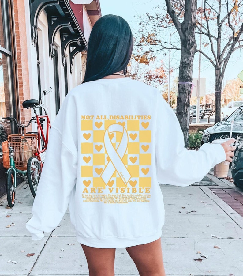 May include: White sweatshirt with a yellow and white checkered pattern and a yellow ribbon with the text "Not all disabilities are visible" printed on the back.