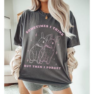 May include: A dark gray t-shirt with a pink graphic of two rabbits and the text "Sometimes I think but then I forget".