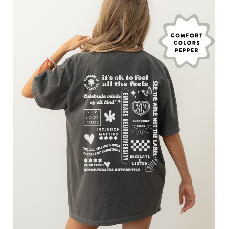 K&ouml;nnte beinhalten: Ein dunkelgraues T-Shirt mit wei&szlig;em Text und Grafiken. Der Text beinhaltet "it's ok to feel all the feels", "Celebrate minds of all kind", "Embrace Neurodiversity", "See the able not the label", "Your words matter", "Inclusion matters", "We all thrive under different conditions", "Everyone communicates differently", "Everybody stims", "Regulate & listen", und "Grind".