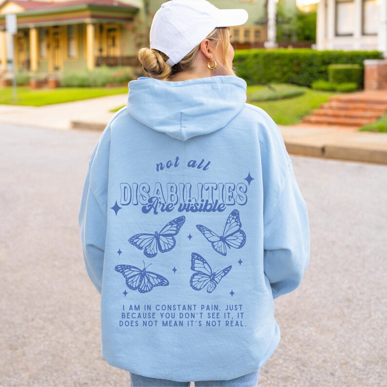 Pu&ograve; includere: Felpa blu chiaro con un messaggio che recita "not all disabilities are visible" e quattro grafiche di farfalle blu. Il testo sotto le farfalle recita "I am in constant pain. Just because you don't see it, it does not mean it's not real."