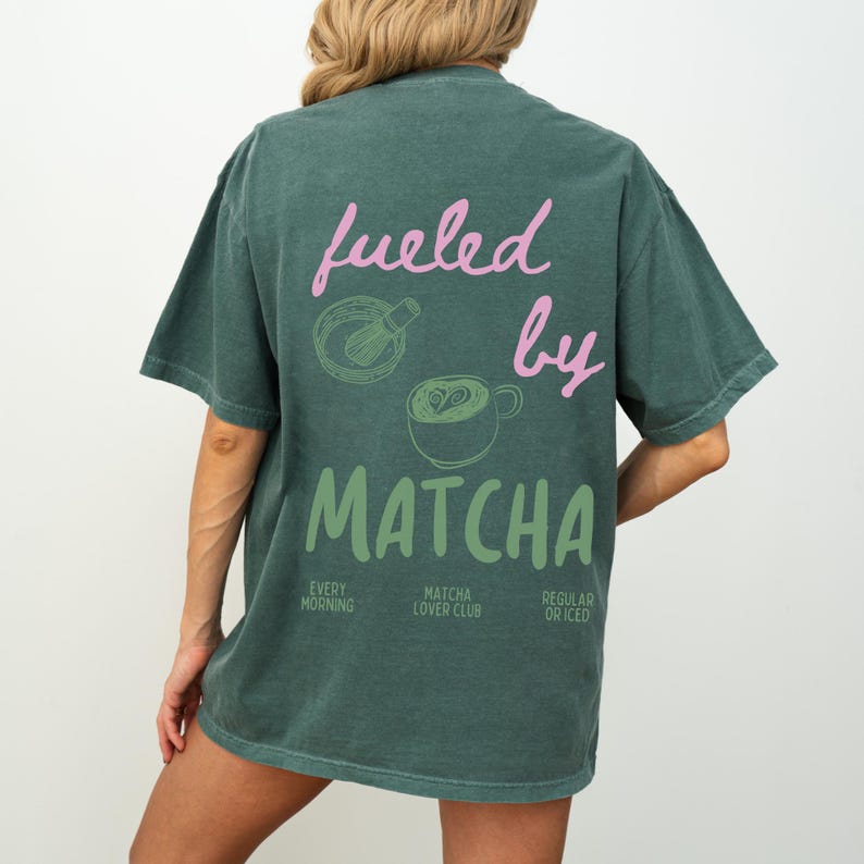 May include: A teal green t-shirt with the text "fueled by matcha" in pink and green. The design includes a matcha whisk and a cup of matcha latte. The text "every morning", "matcha lover club", and "regular or iced" is also included in smaller font.