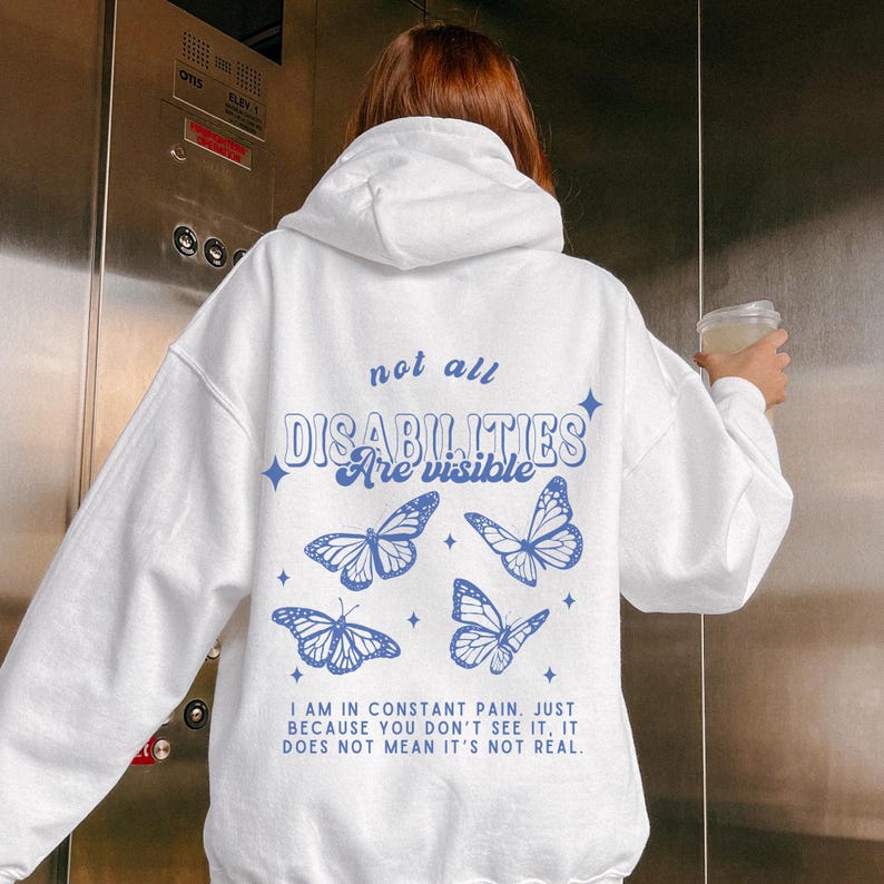 Pu&ograve; includere: Felpa bianca con una grafica di farfalla blu e il testo "not all disabilities are visible". Il testo sotto la grafica dice "I am in constant pain. Just because you don't see it, it does not mean it's not real."