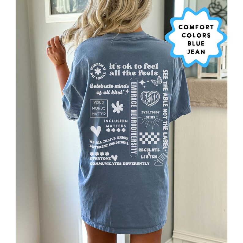 K&ouml;nnte beinhalten: Ein blaues Jeans-T-Shirt mit wei&szlig;em Text und Grafiken. Der Text beinhaltet "it's ok to feel all the feels", "Celebrate minds of all kind", "Embrace Neurodiversity", "See the able not the label", "Your words matter", "Inclusion matters", "We all thrive under different conditions", "Everybody stims", "Regulate & Listen", und "Everyone communicates differently".