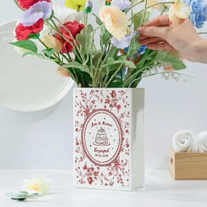May include: A rectangular white ceramic vase featuring a red floral pattern and a central oval frame. The frame contains a line drawing of a tiered cake with the text Joe & Karen, Engaged, and the date 05.15.2026 printed in red ink.