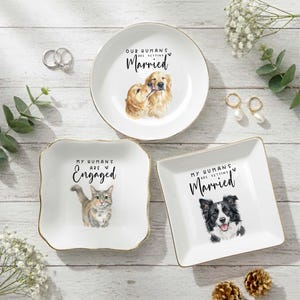 May include: Three white ceramic ring dishes with gold rims. One dish features a Golden Retriever illustration and the text "Our Humans Are Getting Married." Another has a cat illustration and the text "My Humans Are Engaged." The third dish has a Border Collie illustration and the text "My Humans Are Getting Married."