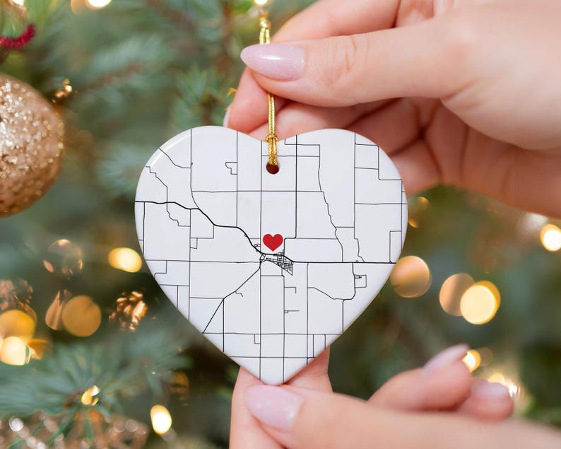 Puede incluir: Adorno de cer&aacute;mica en forma de coraz&oacute;n con un dise&ntilde;o de mapa y un coraz&oacute;n rojo que marca una ubicaci&oacute;n. El adorno blanco tiene l&iacute;neas negras que representan las calles y un coraz&oacute;n rojo. Se adjunta una cuerda dorada para colgar.