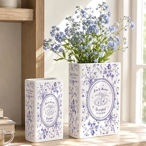 May include: Two rectangular white ceramic vases featuring a blue floral pattern. The vases are personalized with the text 'Joe & Karen', 'Engaged', and the date '05.15.2026' inside an oval frame with two heart-shaped rings and a ribbon bow.
