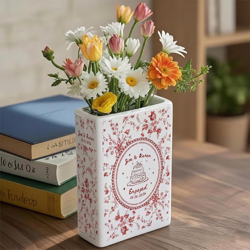 May include: A rectangular white ceramic vase featuring a red floral pattern and a central circular emblem with the text Joe & Karen, a cake illustration, and the word Engaged with the date 05.15.2024, filled with a colorful bouquet of fresh flowers.