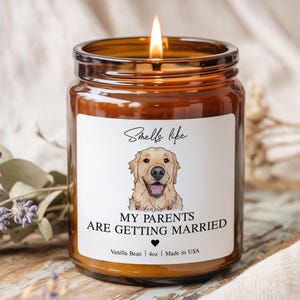 May include: A lit, amber-colored glass jar candle with a white label. The label features a watercolor illustration of a golden retriever and the text "MY PARENTS ARE GETTING MARRIED." The candle is scented with vanilla bean and is 4oz.