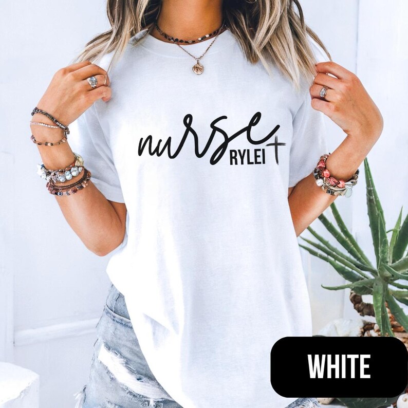 Puede incluir: Camiseta blanca con la palabra "nurse" en fuente cursiva, seguida de "Rylei" y una cruz. La palabra "WHITE" est&aacute; en un rect&aacute;ngulo negro en la esquina inferior derecha.