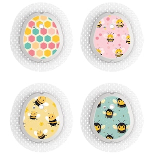 Puede incluir: Cuatro vendajes adhesivos redondos con diferentes diseños de temática de abejas. Los diseños incluyen un patrón de panal, lunares rosas con abejas, estrellas amarillas con abejas y rayas verdes y azules con abejas.