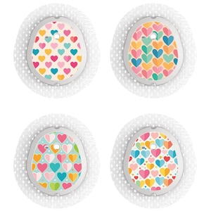 Op de afbeelding: Vier ronde, witte pleisters met kleurrijke hartpatronen. Elke pleister heeft een klein gaatje in het midden.