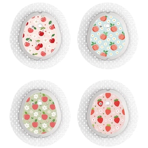 Op de afbeelding: Vier ronde, witte pleisters met verschillende fruitpatronen. Elke pleister heeft een wit midden met een rood kersen-, perzik- of aardbeienpatroon op een lichtblauwe, groene of roze achtergrond.