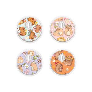 Puede incluir: Cuatro pop sockets redondos, blancos y transparentes con diseños de hámsteres de dibujos animados. Cada pop socket presenta un color de fondo diferente: marrón claro, rosa, lavanda y naranja. Los hámsteres llevan gafas de sol, coronas de flores y sostienen flores.