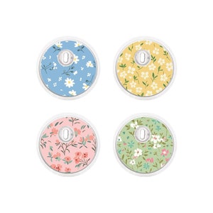 May include: Four round floral fabric covered buttons in pastel colors. Each button features a different floral pattern: blue with white flowers, yellow with white flowers, pink with red flowers, and green with white and pink flowers.