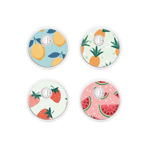Op de afbeelding: Vier ronde stickers met verschillende fruitontwerpen. De stickers tonen citroenen, ananas, aardbeien en watermeloenen op een lichtblauwe, groene, witte en roze achtergrond.