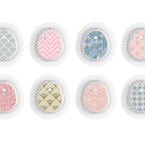 May include: A set of eight oval adhesive patches for medical sensors, each featuring a unique pattern including scallops, chevrons, geometric shapes, floral motifs, paisley, fan designs, and houndstooth in various colours like pink, blue, grey, and gold.