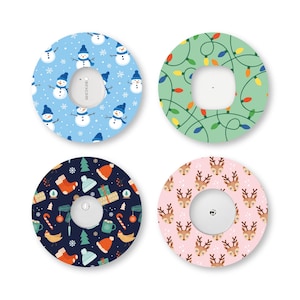 May include: Four circular adhesive patches for medical devices, each featuring a distinct holiday pattern: blue with snowmen, green with colourful string lights, dark blue with winter icons, and light pink with repeating reindeer faces.