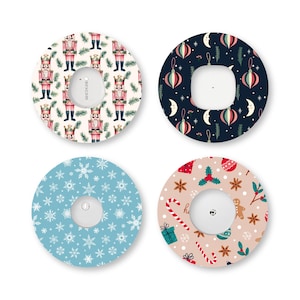May include: Four circular adhesive patches for medical sensors, each featuring a distinct holiday pattern: nutcrackers on cream, ornaments and moons on navy, white snowflakes on light blue, and gingerbread men with candy canes on beige.