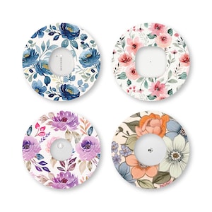 Può includere: Quattro cerotti adesivi circolari per sensori medici, ognuno con un motivo floreale distinto. I disegni includono fiori in stile acquerello blu, rosa, viola e arancioni con foglie verdi su sfondo bianco, che circondano un'apertura centrale.
