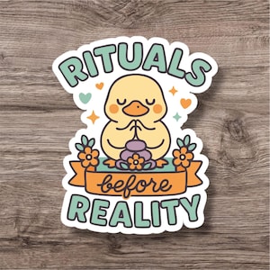 Puede incluir: Una pegatina con un pato de dibujos animados meditando, con el texto "RITUALS before REALITY". El pato es amarillo con detalles naranjas, y el texto es en turquesa con una pancarta naranja. La pegatina tiene un borde blanco y está decorada con corazones y estrellas.