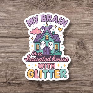 Puede incluir: Una pegatina con el texto "MY BRAIN is a haunted house WITH GLITTER". La pegatina presenta una casa encantada de dibujos animados con fantasmas, un murciélago y estrellas. La casa es de color turquesa con detalles morados, y el texto es de varios colores.