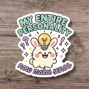 Może przedstawiać: Naklejka z kreskówkowym królikiem i żarówką, z napisem "MY ENTIRE PERSONALITY now makes sense". Projekt zawiera gwiazdki i znaki zapytania. Naklejka ma białą obwódkę i jest w zabawnym stylu.