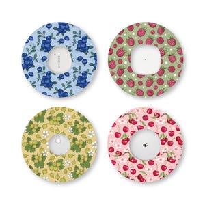 May include: Four circular adhesive patches for medical devices, each featuring a distinct fruit pattern. The designs include blue blueberries on a light blue background, red raspberries on green, green gooseberries on yellow, and red cherries on pink.
