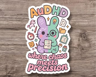 May include: A sticker featuring a split-colored bunny with the text "AuDHD where chaos meets precision." The bunny is half purple and half green, holding a checklist. Surrounding the bunny are various small illustrations, including a unicorn and a lightbulb.