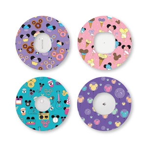May include: Four circular adhesive patches for medical devices, each featuring a distinct pattern. Designs include purple with donuts and cupcakes, pink with ice cream cones, teal with retro icons, and purple with balloons, all featuring mouse ear shapes.