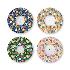 May include: Four circular adhesive patches for medical sensors, each featuring a distinct floral pattern. The designs include a dark blue background, a beige background, a dark green background, and a light pink background, all with colorful flowers.