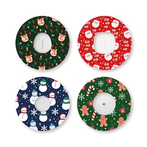 Peut inclure: Quatre patchs adhésifs circulaires pour dispositifs médicaux avec des motifs de fêtes. Un vert foncé avec des rennes, un rouge avec des visages de Père Noël et le texte HO HO HO, un bleu marine avec des bonhommes de neige, et un vert avec des bonshommes en pain d'épice.
