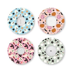 May include: Four circular adhesive patches for medical devices, each featuring distinct Halloween patterns: white ghosts on blue, orange and pink pumpkins on cream, skulls and witch hats on pink, and ghosts with bows on light green.