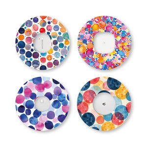 Puede incluir: Cuatro parches adhesivos circulares para dispositivos médicos, cada uno con un patrón único de estilo acuarela de puntos multicolores en tonos azul, rosa, naranja y amarillo, rodeando un área central recortada de color blanco.